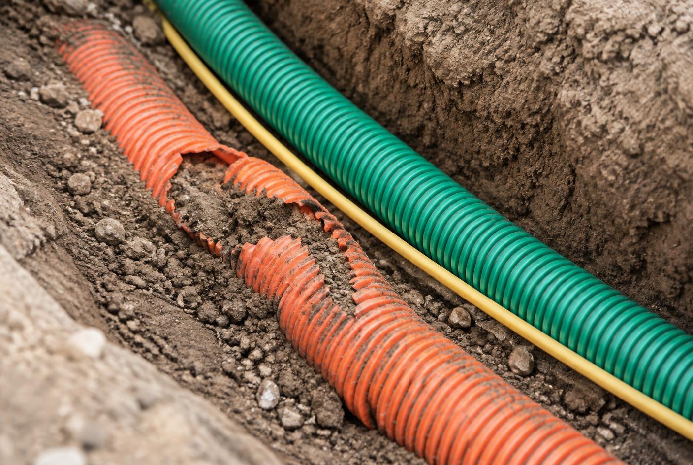 Gaine télécom orange endommagée près d'une gaine verte dans une fouille